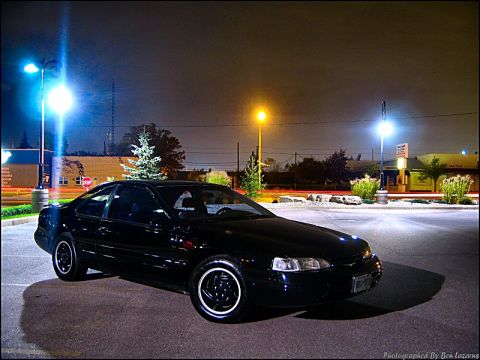 1997 Ford Thunderbird - A black coupe is parked in a lot at night, illuminated by streetlights.