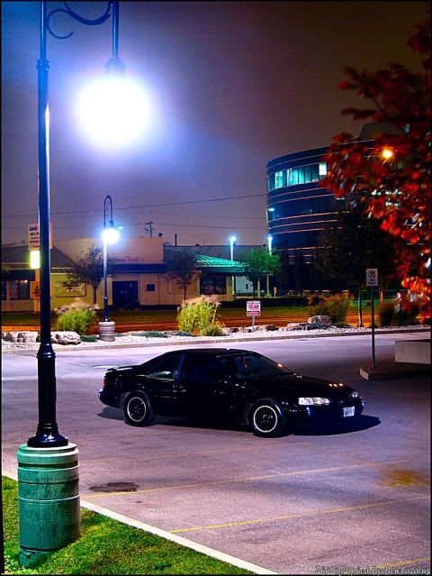 1997 Ford Thunderbird - A black 1997 Ford Thunderbird is parked in a lot at night, illuminated by a street lamp.