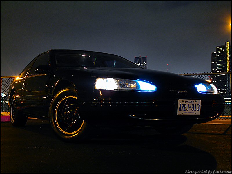 Black 1997 Ford Thunderbird 3q-front view at night with blue headlight accents
