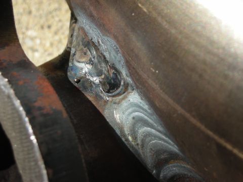 1992 Ford Crown Victoria - Extreme close-up of a fresh stack-of-dimes weld bead joining a steel bracket to a curved axle or housing tube, the metal still showing heat…