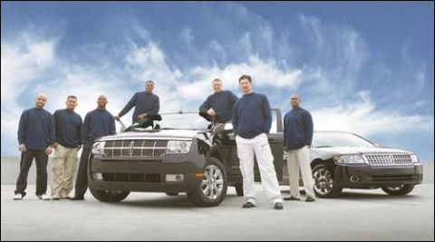 1971 Ford Ranchero - Several men pose with two dark sedans under a cloudy blue sky.
