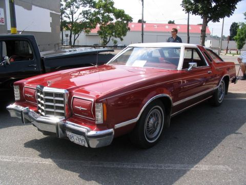 1993 Ford Taurus - A red 1977-1979 Ford Thunderbird coupe is parked next to a black pickup truck at an outdoor car show.