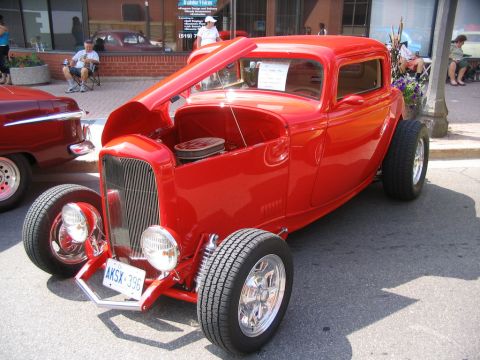 1993 Ford Taurus - A red hot rod coupe is displayed at a car show, with its hood open. Another vehicle is partially visible.