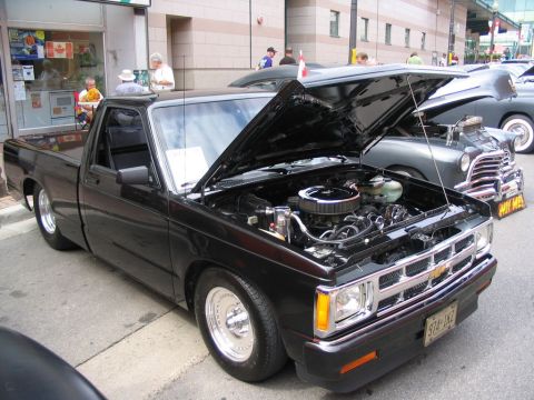 1993 Ford Taurus - A black pickup truck is displayed with its hood open, revealing the engine, at an outdoor car show.