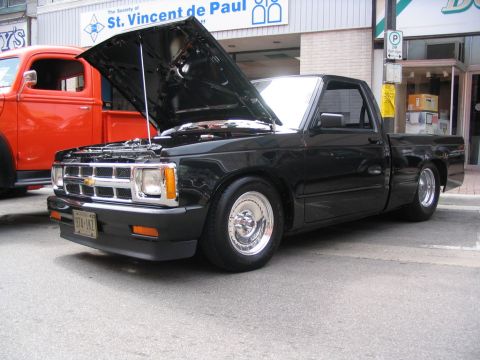 1993 Ford Taurus - A black pickup truck is parked on a street with its hood open, next to an orange truck.