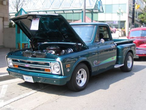 1993 Ford Taurus - A classic green Chevrolet pickup truck is displayed with its hood open, parked on a street next to another vehicle.