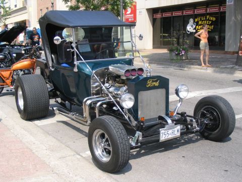 1993 Ford Taurus - A custom hot rod with a Ford badge and exposed engine is parked on a city street.