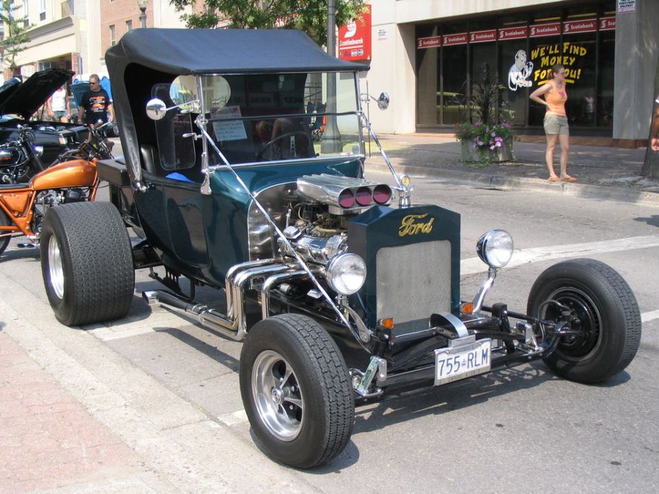 Dark green hot rod with a Ford badge, exposed engine, and large rear tires