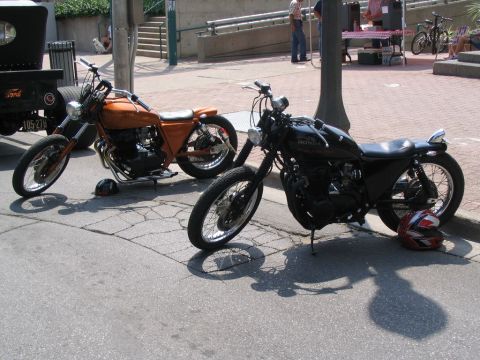1993 Ford Taurus - Two custom motorcycles, one orange and one black, are parked on a cracked asphalt street.