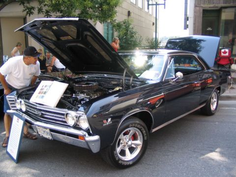 1993 Ford Taurus - A man looks at the engine of a black 1967 Chevrolet Chevelle SS at a car show.