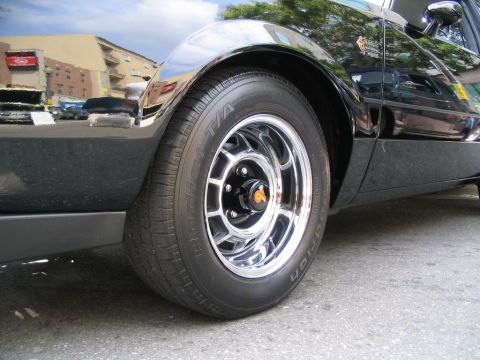 1993 Ford Taurus - A black car with chrome wheels is parked on asphalt, reflecting buildings in its glossy finish.