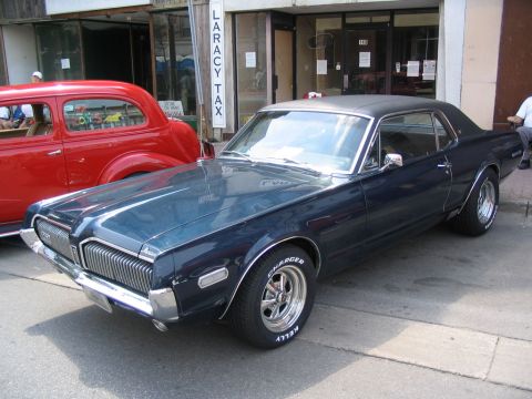 1993 Ford Taurus - A dark blue 1968 Mercury Cougar is parked next to a red car at a car show.