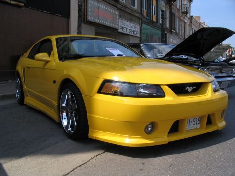1993 Ford Taurus - A bright yellow Ford Mustang is parked on a street in front of buildings, with another car behind it.