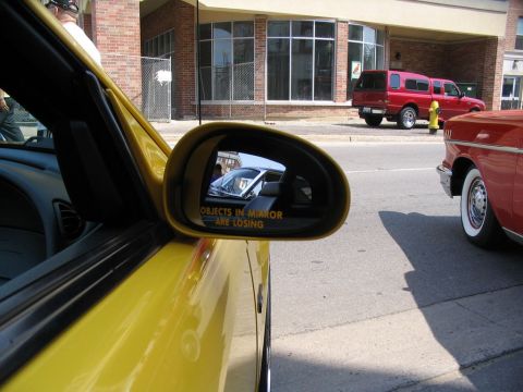 1993 Ford Taurus - A yellow car's side mirror shows a reflection of a white car's interior and a warning about objects in the mirror.