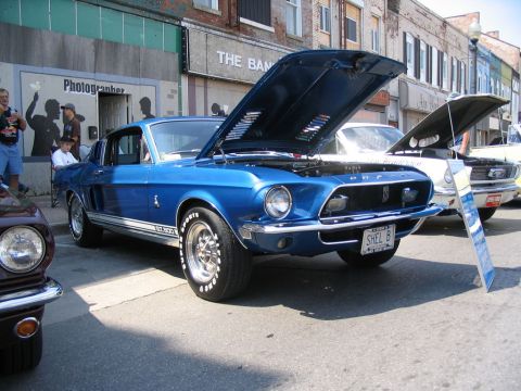 1993 Ford Taurus - Blue 1967 Shelby GT500 Mustang at a car show, hood open, with other vehicles present.