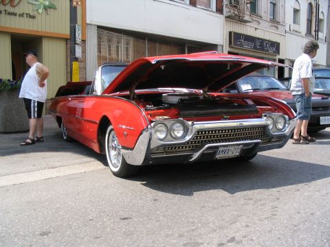 1993 Ford Taurus - A red convertible, likely a 1961 model, is displayed with its hood open at a car show.