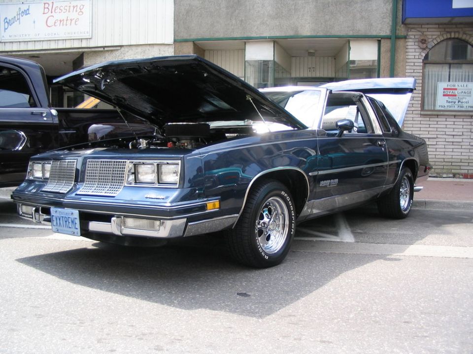 dark blue coupe with hood and trunk open, parked next to a dark pickup truck