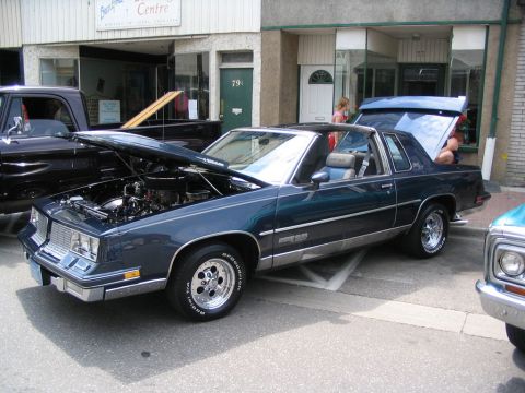1993 Ford Taurus - A dark blue coupe is displayed with its hood and trunk open at a car show.
