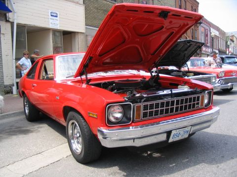 1993 Ford Taurus - A red 1975 Chevrolet Nova coupe is displayed with its hood open at a car show, with other vehicles visible in the background.