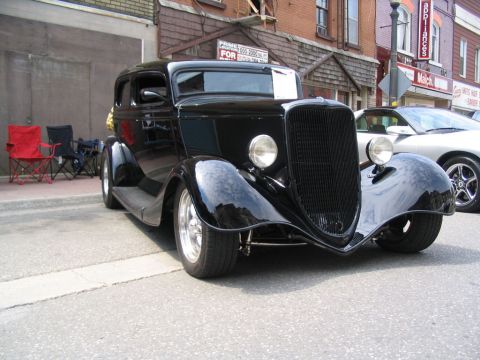 1993 Ford Taurus - A black hot rod with a prominent grille is parked on a street next to a modern silver car.