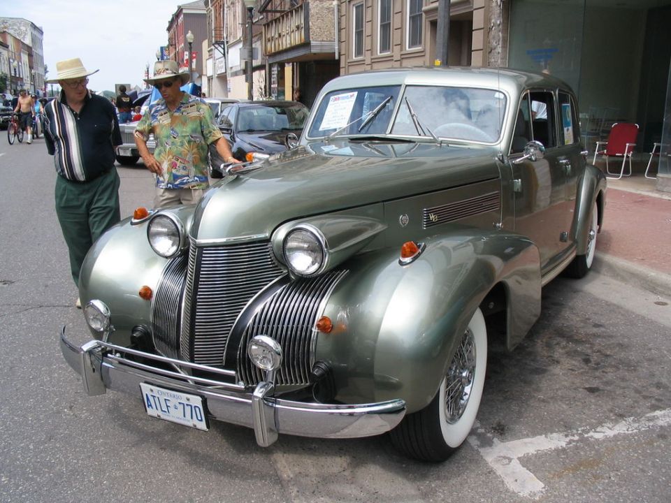 Green vintage car with chrome grille and whitewall tires, parked on street