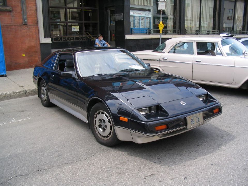 Black Nissan 300ZX with a license plate that reads '86 ZX'. Another car is parked behind it