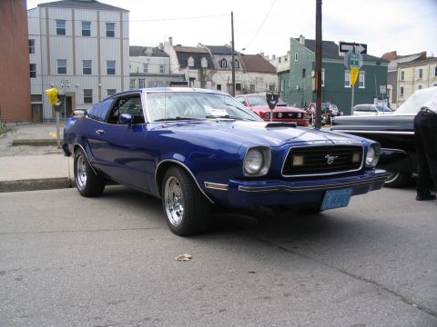 1993 Ford Taurus - A blue 1970s Ford Mustang II is parked on a street, with other vehicles visible in the background.