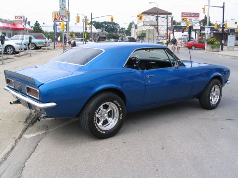 1993 Ford Taurus - Blue 1967 Chevrolet Camaro parked on a city street with buildings in the background.