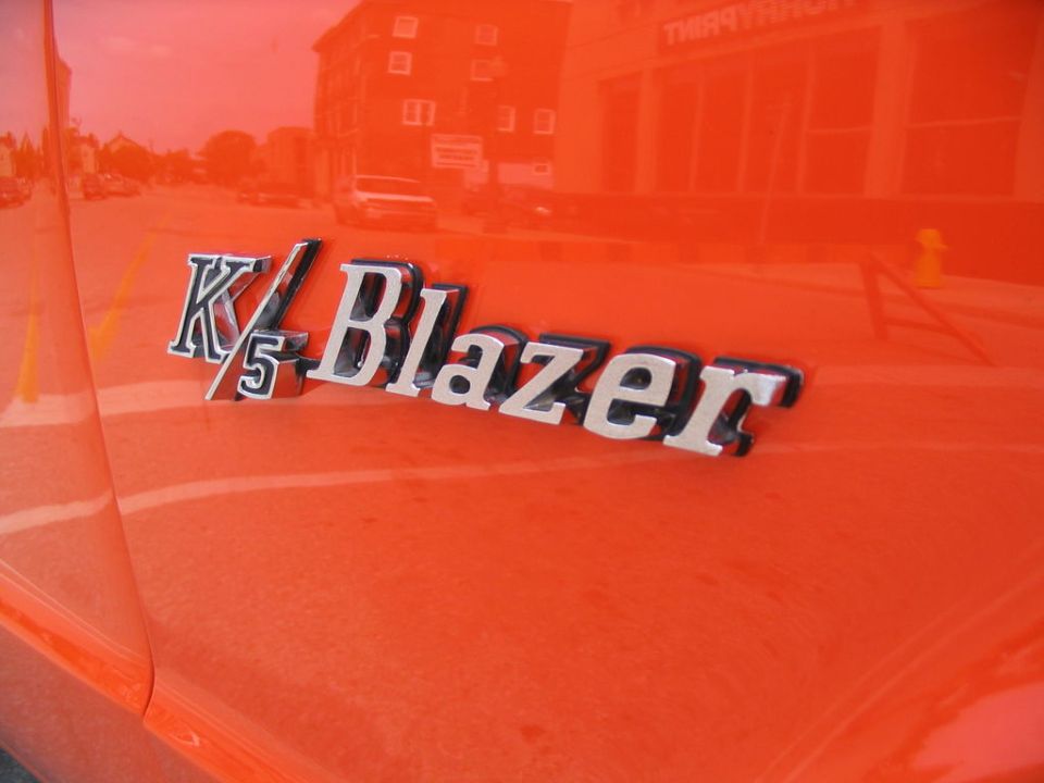 Orange vehicle side panel with K/5 Blazer emblem. Reflections show buildings and street