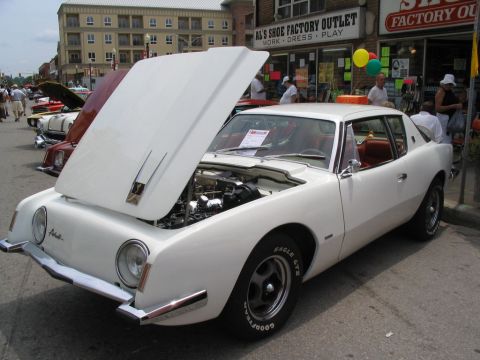 1993 Ford Taurus - A white 1963 Studebaker Avanti is displayed with its hood open at a car show.