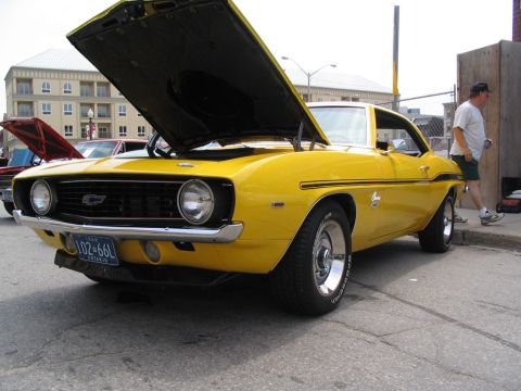 1993 Ford Taurus - A yellow 1969 Chevrolet Camaro is displayed with its hood open at a car show. Another car with its hood open is visible behind it.