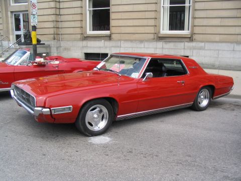 1993 Ford Taurus - A red coupe is parked on the street next to a red convertible.