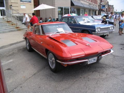 1993 Ford Taurus - A red 1963 Chevrolet Corvette coupe is parked on a street next to other vehicles at a car show.