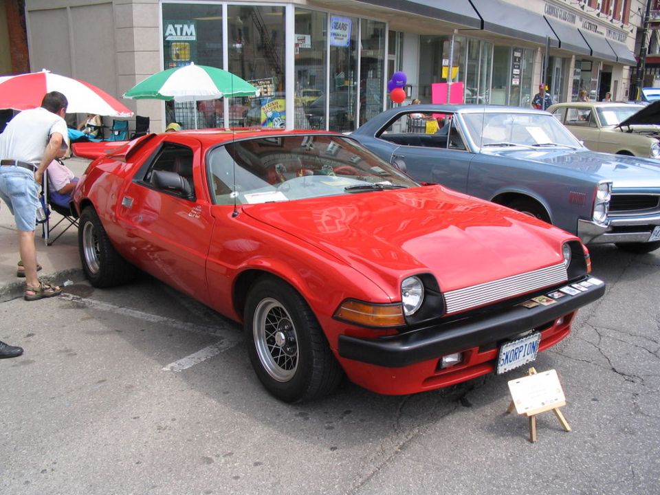 Red AMC Pacer with a license plate that reads 'SKORPION', parked next to a blue car