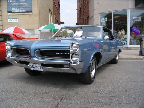 1993 Ford Taurus - A light blue Pontiac Tempest is parked on a city street, with a red car visible behind it.