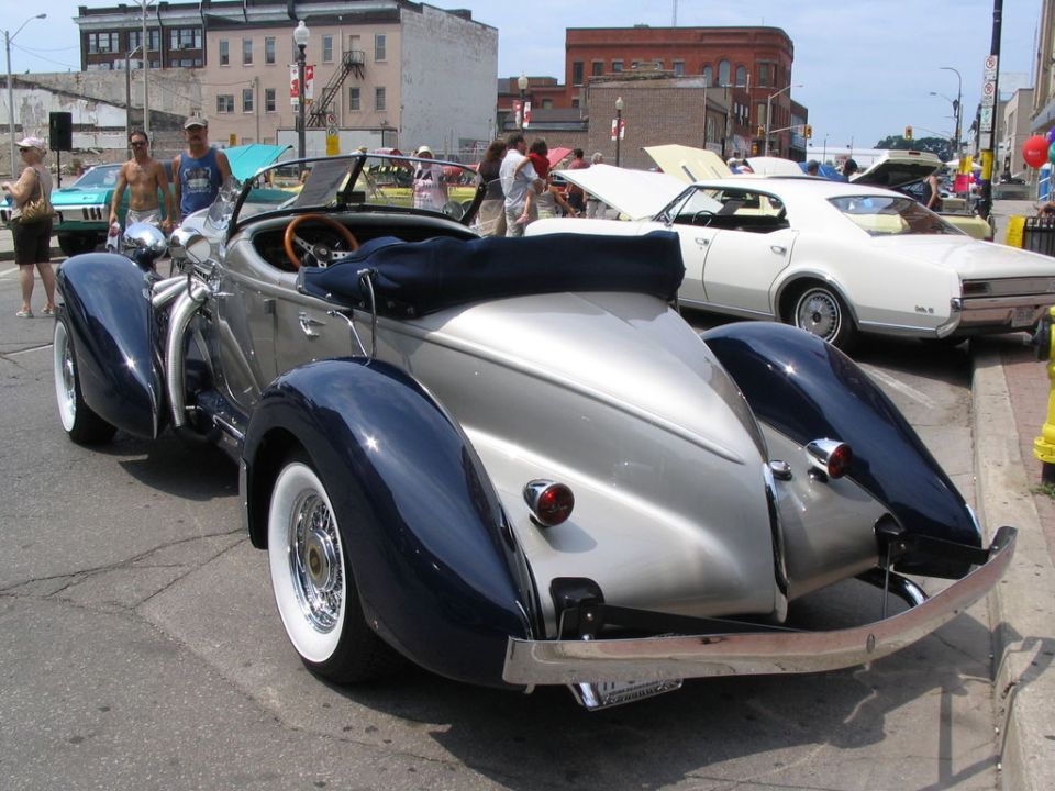 Silver and blue convertible with whitewall tires, rear view