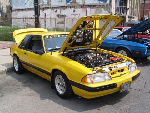 1993 Ford Taurus - Yellow coupe with engine exposed at a car show, with another vehicle visible behind it.