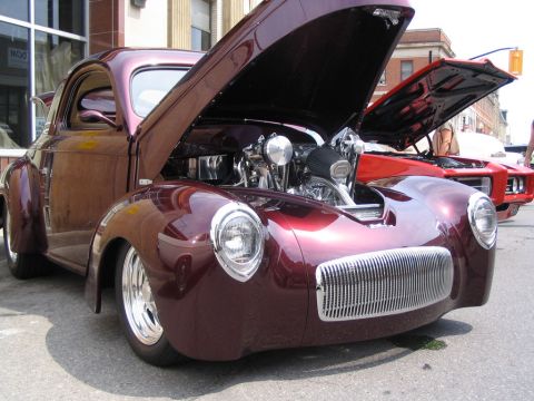 1993 Ford Taurus - A custom hot rod coupe is displayed with its hood open, revealing a powerful engine, at a car show.