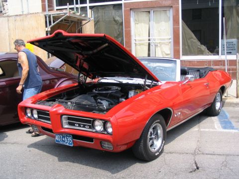 1993 Ford Taurus - A red 1969 Pontiac GTO convertible is displayed with its hood open, revealing the engine. Another classic car is parked alongside.