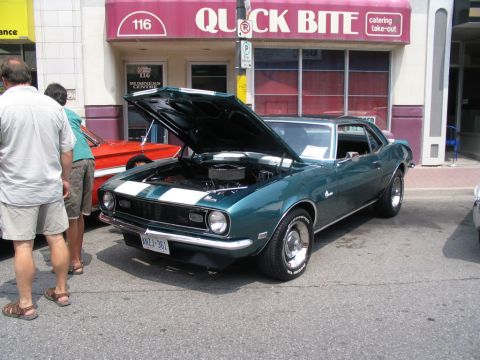 1993 Ford Taurus - Green 1968 Chevrolet Camaro displayed at a car show with its hood open, parked next to a red car.