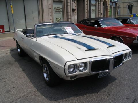1993 Ford Taurus - A white 1969 Pontiac Firebird convertible with blue racing stripes is parked on a street next to other cars.