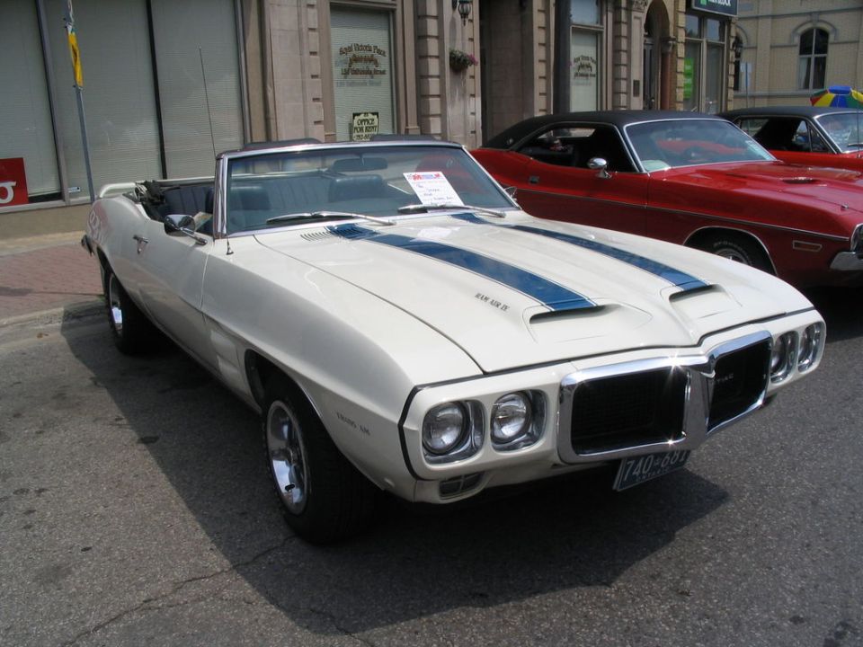 White 1969 Pontiac Firebird convertible with blue stripes, chrome grille, and fender badges, parked on street
