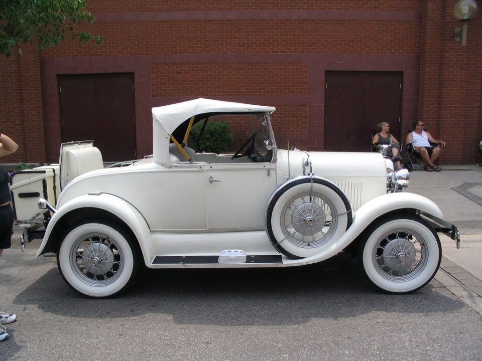 White convertible with a spare tire on the side, parked outside a brick building