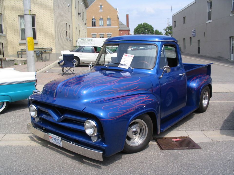 Blue 1956 Ford F-100 pickup with flame paint job parked on street