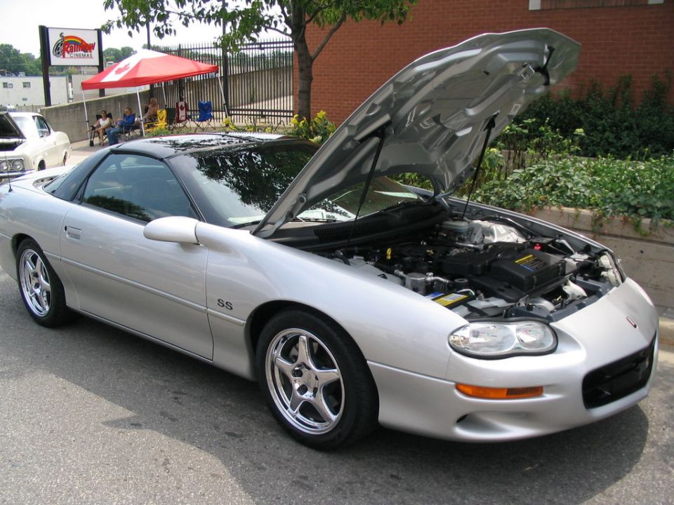 Silver Chevrolet Camaro SS with hood open, showing engine. Chrome five-star wheels. "SS" badge visible