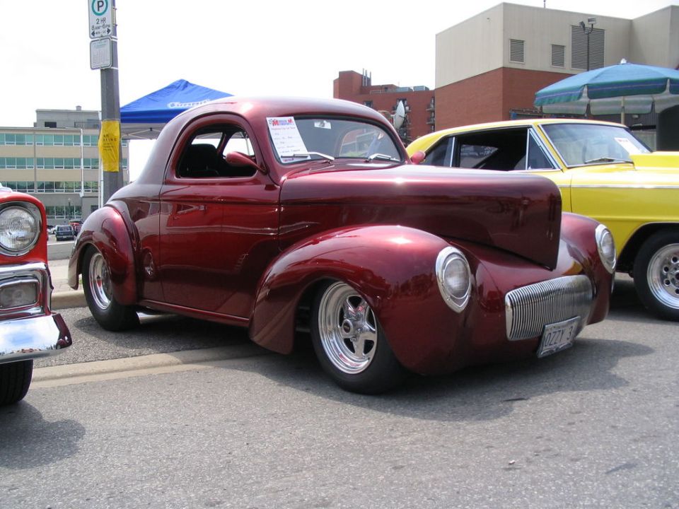 Red hot rod coupe with custom grille and lowered stance parked next to a yellow car