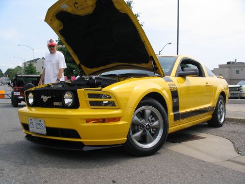 1993 Ford Taurus - Yellow Ford Mustang with 'BOSS 302' badging and racing stripes, hood open at a car show.