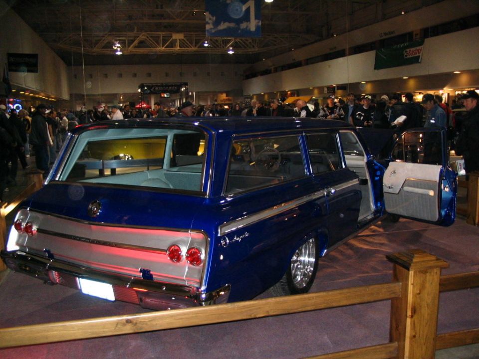 Blue station wagon with chrome trim and custom wheels, doors open, inside a building with people around