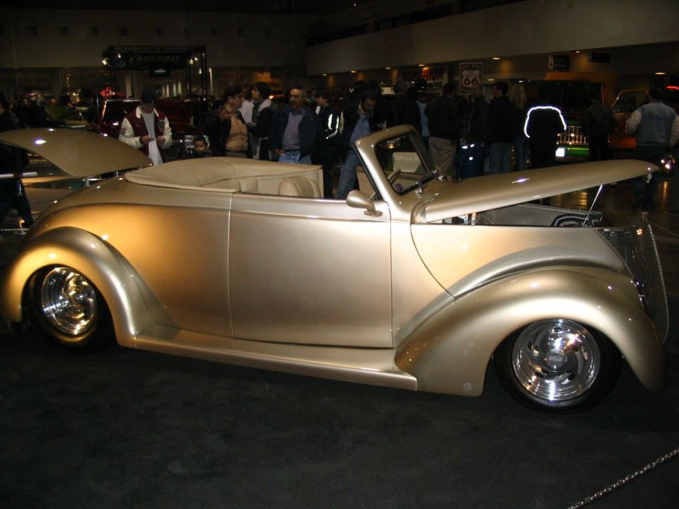 Gold convertible with hood open, custom wheels, tan interior, at a car show