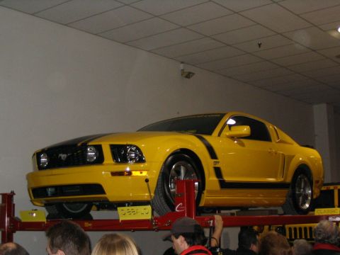 1993 Ford Taurus - A yellow Ford Mustang GT is displayed on a lift, showing its distinctive racing stripes and GT badging.